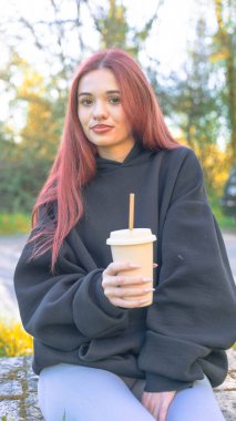 Parkta oturmuş kapaklı bir bardaktan samanla içki içen genç bir kızıl. Rahat ve doğal bir yaşam tarzı olan sıradan bir açık hava sahnesi..