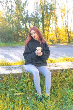 Parkta oturmuş kapaklı bir bardaktan samanla içki içen genç bir kızıl. Rahat ve doğal bir yaşam tarzı olan sıradan bir açık hava sahnesi..