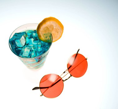 Limon dilimi ve temiz bir arkaplanda yuvarlak güneş gözlüğüyle süslenmiş mavi buzlu bir içeceği içeren canlı bir yaz konsepti..