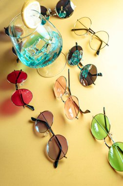 Bej arka planda, buzlu ve limon dilimli mavi bir kokteyl etrafında retro-stil güneş gözlüklü yaz kompozisyonu.