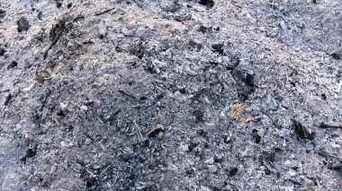 Kömür kalıntılarıyla birlikte beyaz ve siyah odun külü yığınının yakın görüntüsü, yanmadan sonra kaba doku ve doğal desenleri gösteriyor.