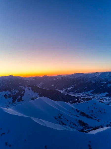 Vertical aerial panorama of snowy mountain ridge on winter sunrise. Stunning mountains range covered with snow powder on ski resort at sunset. Caucasus mountain peaks skyline in a dusk golden hour.