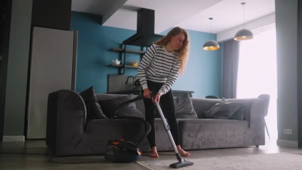 年轻的卷曲高加索女人吸尘地板在她的公寓 在现代时尚公寓里 成年女性用真空吸尘器清洁地毯 打扫房子的过程 家庭主妇打扫房间里的烂摊子 — 图库视频影像