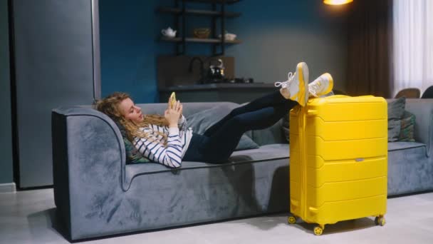Traveller Γυναίκα Χαλαρώστε Ξαπλωμένη Στον Καναπέ Πόδια Κίτρινο Τροχοφόρο Βαλίτσα — Αρχείο Βίντεο