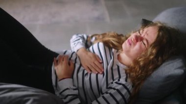 Oturma odasındaki kanepede oturan beyaz kadın kalp ağrısı çekiyor. Çok kötü hissediyor. Genç bir kadın göğsünde şiddetli bir ağrı hissediyor. Kız ani kalp ağrısından muzdarip.