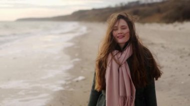 Deniz kıyısında gülümseyen ve kameraya bakan mutlu etnik kız. Okyanus kıyısında durup gülen neşeli Asyalı kadının portresi. Rüzgâr onun havadar saçlarını savuruyor. Hayali sinematik ağır çekim.