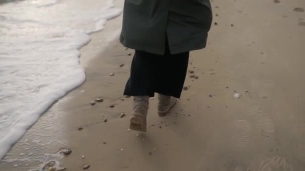 해변에서 달아난 여인의 뒷모습 아름다운 코트를 베이지 부츠를 파도와 거품으로 — 비디오