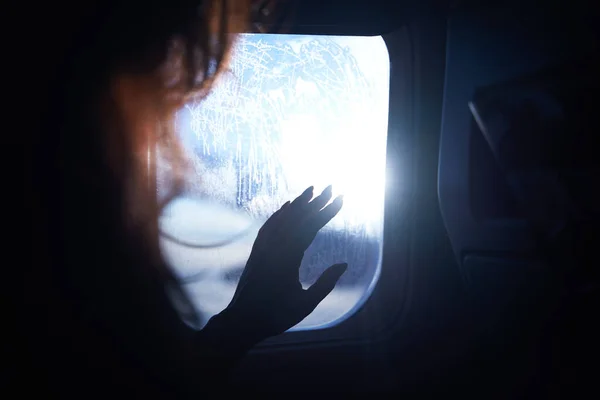 Female hand touches the warm sun rays from airplane window. Woman looking forward to travel on her vacation. Girl on a journey flight sitting in an aircraft and enjoys sun flares.