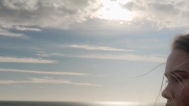 Karmaşık, hüzünlü, karamsar, karamsar, rüzgarlı bir günde deniz manzarası seyreden bir kadın. Depresyonda olan düşünceli bir kadın okyanus kenarında fazla düşünüyor. Rüzgâr havadar saçlar savuruyor. Çekim ayarlanıyor.