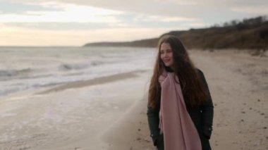 Mutlu gülümseyen kadın sonbahar günü kumlu sahilde dalgalar boyunca yürür. Yeşil ceketli, sosyetik, melez bir kadın okyanus kıyısına doğru gidiyor. Hayalci, parlak, sinematik, ağır çekim..