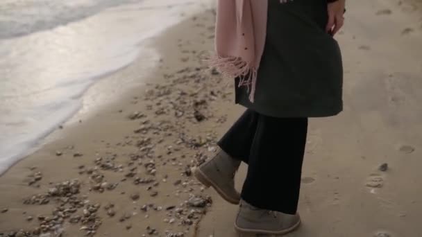砂の海のビーチで逃げ幸せな女性のバックビュー スタイリッシュな緑のコートに身を包んだ少女 ベージュのブーツ 波と泡によって洗浄海岸線に沿って実行しています スローモーションでの夢のような映画撮影 — ストック動画