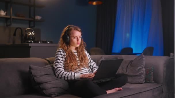 Γυναίκα Στα Ακουστικά Λειτουργεί Φορητό Υπολογιστή Από Σπίτι Και Απολαμβάνει — Αρχείο Βίντεο
