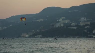 Güzel bir günbatımında mavi denizin üzerinde paraşüt çeken bir tekne. Sürat teknesi, deniz boyunca ufukta turistlerle paraşüt çekiyor. Durgun suda parasailing. Ekstrem spor havası.
