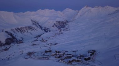 Kayak merkezinde kış gündoğumunda karlı dağ sırasının havası. Dağların üstündeki ay vadisi ve köyü gün batımında yol değiştiriyor. Kafkaslar alacakaranlıkta ufuk çizgisi oluşturur. Gece şehir ışıkları.
