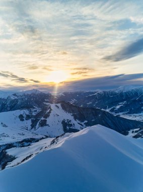 Gün doğumunda kayak köyünde karlı dağ sırasının geniş hava manzarası. Gün batımında kayak merkezinde kar tozu kaplı sersemletici dağlar. Kafkasya dağlarının tepeleri gün batımında ufuk çizgisi.