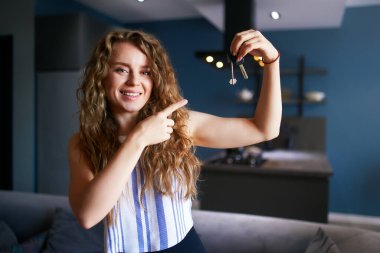 Modern iç mekanlarda yeni ev ya da dairenin anahtarlarını gösteren mutlu bir kadın. Yeni ev anahtarlarıyla kiracı kadın kiracı taşınıyor. Bayan taşınmak için emlak satın almış. Bir mülkiyet kavramı.
