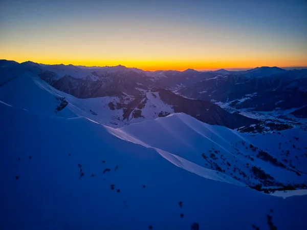Vertical aerial panorama of snowy mountain ridge on winter sunrise. Stunning mountains range covered with snow at sunset afterglow. Caucasus mountain peaks skyline in a twilight golden hour.