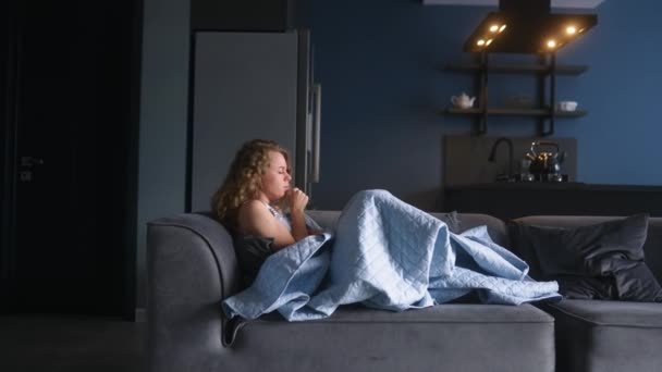 患流感的妇女咳嗽着 在家里的沙发上用毯子捂住鼻子 年轻的高加索女性在隔离的过程中患上了高头牛Covid19 生病的女孩躺在沙发上挣扎寒冷 — 图库视频影像