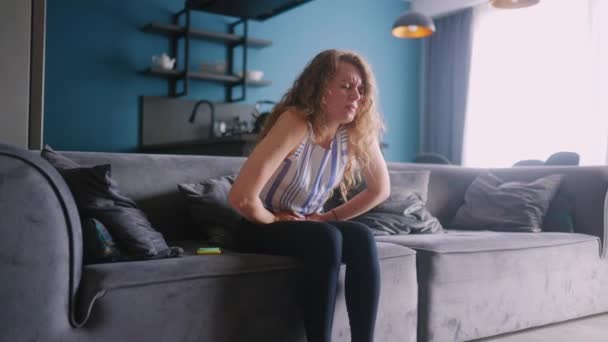 患严重胃痛的白人妇女坐在客厅的沙发上 感到非常恶心 经历经期抽筋的年轻成年女性 得了急性膀胱疼痛的女孩 — 图库视频影像