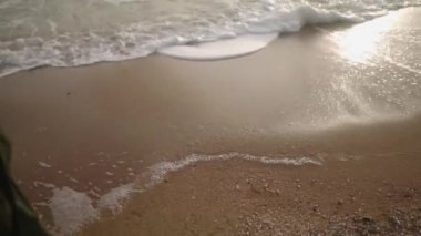 Kumlu sahilde deniz dalgaları köpüğü boyunca yürüyen çizmeli kadın ayakları. Yeşil ceketli bir kadın, kıyı şeridinde okyanus gelgitleri boyunca gider. Rüya gibi sinematik dekişiselleştirilmiş çekim kuruyorum..