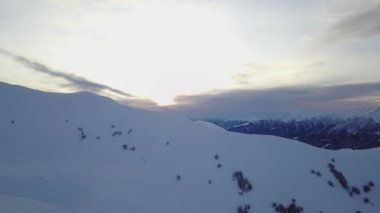 Gün doğumunda kayak köyünde karlı dağ sırasının geniş hava manzarası. Gün batımında kayak merkezinde kar tozu kaplı sersemletici dağlar. Kafkasya dağlarının tepeleri gün batımında ufuk çizgisi.