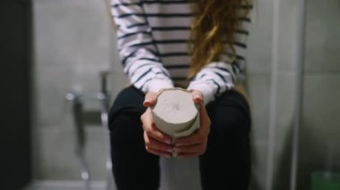 Kadın vücudunun alt kısmı tuvalette oturuyor ve ishal ve mide ağrısından muzdarip. Kadın hemoroit yığınları yüzünden kaka yapamıyor. Elinde tuvalet kağıdı tutan ve sallayan gergin bir kız..