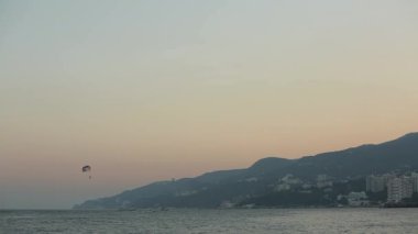 Güzel bir günbatımında mavi denizin üzerinde paraşüt çeken bir tekne. Sürat teknesi, deniz boyunca ufukta turistlerle paraşüt çekiyor. Durgun suda parasailing. Ekstrem spor havası.