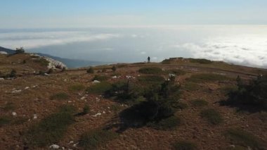 Erkek kaşifin dağların kıyısında kollarını kaldırarak yürüyüş esnasında özgürlüğün tadını çıkardığını gösteren hava görüntüsü. Erkek yürüyüşçü, gün batımında uçurumda tek başına duruyor.
