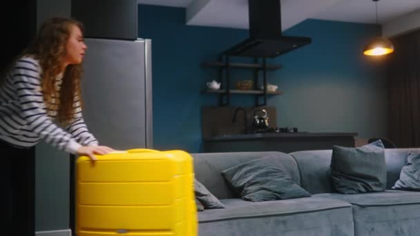 游客妇女在入住酒店后 拖着巨大的黄色轮式行李箱 倒在沙发上休息 女带着行李 躺在租来的公寓里休息 — 图库视频影像