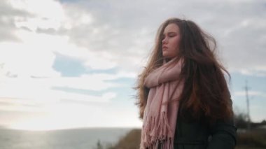 Üzgün düşünceli kadın uçurumun kenarında duruyor ve karamsar bulutlu bir günde deniz manzarasına bakıyor. Depresyondaki düşünceli, yalnız bir kadın, okyanus kenarında fazla düşünen bir ceket giyiyor. Rüzgâr karışık etnik kız saçlarını savuruyor..