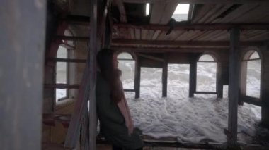 Eski model terk edilmiş bir ev odasında kumlu sahilde gelgit suyunda batan bir kadın. Eski ahşap bir evde duran su basmış, iç kısımları deniz dalgalarıyla yıkanmış bir kadın. Rüya gibi gerçeküstü sinematik görüntüler