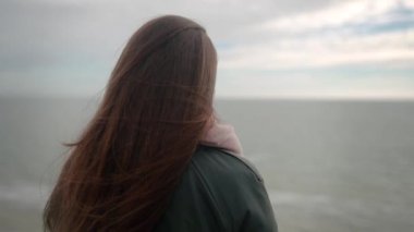 Uçurumun tepesinde dikilip deniz manzarası seyreden melez etnik kadın kasvetli bulutlu bir günde kameraya dönüyor. Düşünceli, uzun saçlı, yeşil paltolu bir kadın okyanus kenarında fazla düşünüyor. Rüzgâr dalgalı saçlar savurur.