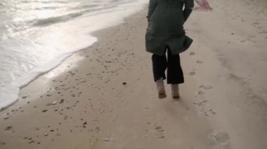 Kumlu deniz sahillerinde koşan mutlu etnik kadın ayakları. Neşeli, gülümseyen, rüzgarda uçuşan havadar kadın saçı. Pov, beni takip et. Yeşil ceketli, pembe atkılı bir kız resmi. Rüya gibi sinematik çekim..