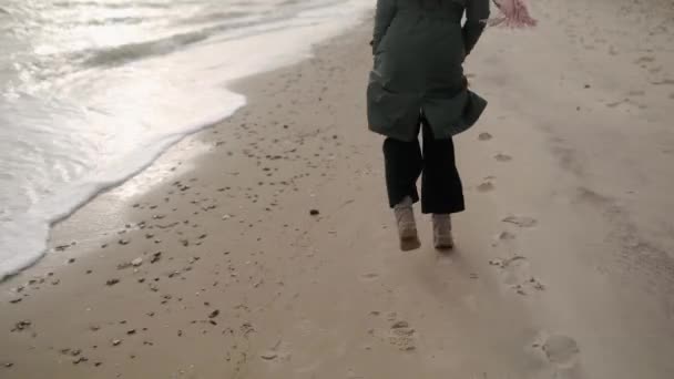 幸せな混合民族の女性の足の砂の海のビーチで実行している 風に吹いて遊び心のある笑顔の女性の風通しの良い髪 ポフは私のスタイリッシュな緑のコート ピンクのスカーフで女の子のショットに従ってください 夢のような映画撮影 — ストック動画