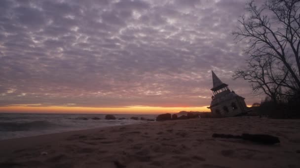 神秘的なヴィンテージは ピンクの夕日の海岸線で海の波に洗われた木の家やチャペルを傾け殺到した 相撲の日の出に防波堤の近くのビーチで水に沈む壮大なレンガ造りの建物 — ストック動画