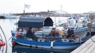 2019-05-01, Cyprus, Larnaka. Fishermen mending their nets on a fishing boat in harbor. Men mending fishing nets on moored boat in marina harbour. People fixing nets, one working on bow.