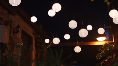 Warm white round glowing lamps swinging on street over head. Motion movement of white orbicular Chinese lanterns. Handmade spheric street lamps swinging and glowing at night. High quality 4k footage