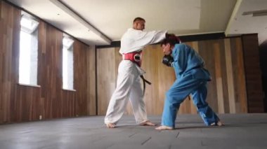Two martial arts men in kimonos and gloves practicing kicks and punches. Male fighters wearing kimono, gloves and protection belts training sparring at gym. Kick boxers jumping and practicing actions