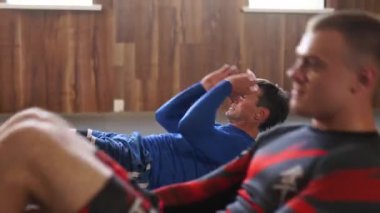 Athletic men at gym doing series of active sit-ups. Fit male fighters in sportswear performing exhausting workout session against the wall. Sportsmen doing sit-ps and crunches