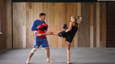 Coach giving private training to female athlete practicing punches. Training sparring of female kickboxer and male trainer practicing punches and kicks. Girl boxing in urban gym. Feminist concept