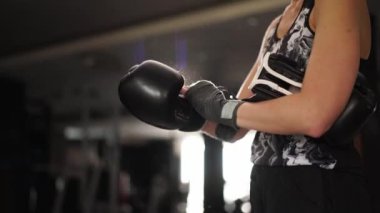 Strong woman puts on black boxing gloves on wrapped fists in gym. Caucasian sports woman wears boxing mittens closeup shot. Getting ready for training in the gym. Strong independent woman concept