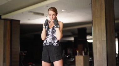 Portrait of sportswoman facing camera looking aggressively. Young sports woman standing in a ready-to-fight posture. Portrait of female boxer with her fists near face seriously looking at camera