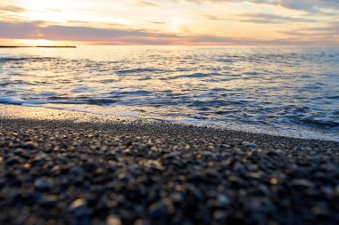 A pure transparent sea wave rolls over the rocky pebble shore, concept of rest and travel, tranquility, relaxation and reflection on a warm summer day, close-up. Small pebbles on the seashore