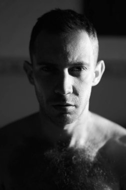 Kameraya bakan sert ışıklı yakışıklı adamın portresi. Çekici erkek yüzünün yarısı güneşin doğuşuyla aydınlanır. Yüksek kaliteli siyah beyaz fotoğraf