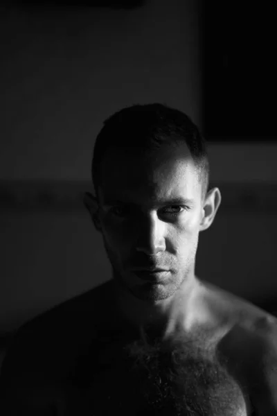 Portrait of handsome man in hard side light facing camera. Half of attractive male face lit by the sun rays on sunrise. High quality black and white photo