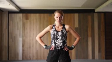 Portrait of a sportswoman facing camera looking confidently. Young sports woman standing with her hands on sides in strong confident posture. Portrait of female boxer serious looking at camera.