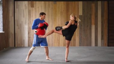 Coach giving private training to female athlete practicing punches. Training sparring of female kickboxer and male trainer practicing punches and kicks. Girl boxing in urban gym. Feminist concept