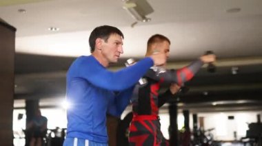 Male boxers training activities with dumbbells in fitness club. Male fighters exhausting box training kicks with dumbbells. Adult and fit men having evening workout indoor. Fitness and sport concept