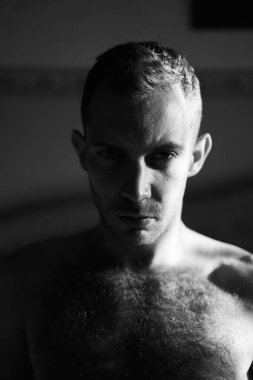 Kameraya bakan sert ışıklı yakışıklı adamın portresi. Çekici erkek yüzünün yarısı güneşin doğuşuyla aydınlanır. Yüksek kaliteli siyah beyaz fotoğraf