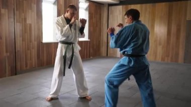 Martial arts men in kimonos practice kicks and punches. Male fighters wearing kimono training in gym. Kick boxers jumping and practicing kicking and punching actions indoors. People and sport concept